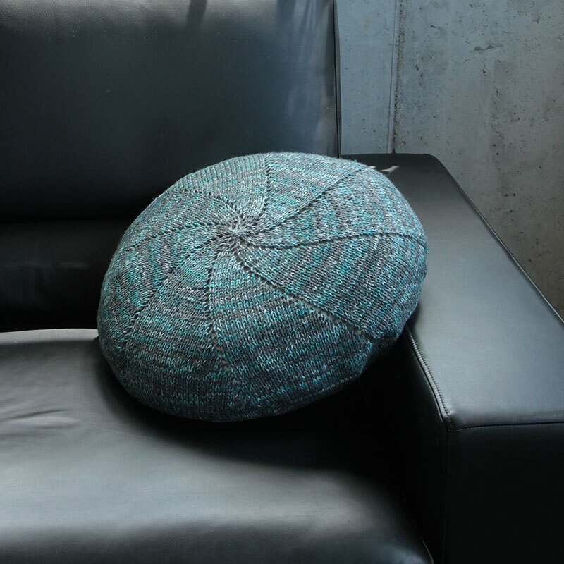 Rundes gestricktes Kissen in Petrol und Grau auf dunklem Sofa