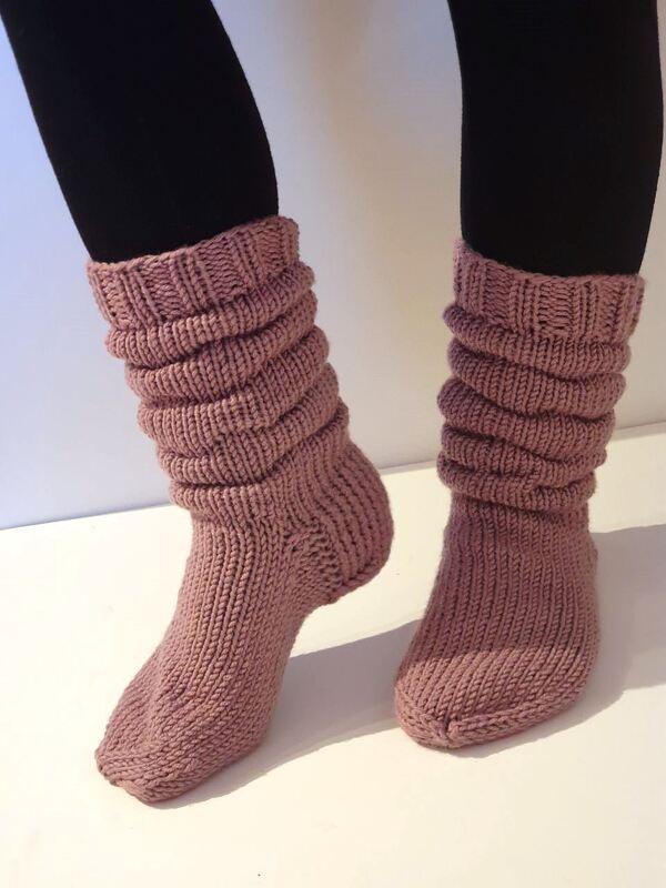 Beine in schwarzen Leggings mit altrosafarbenen, gerafften Stricksocken