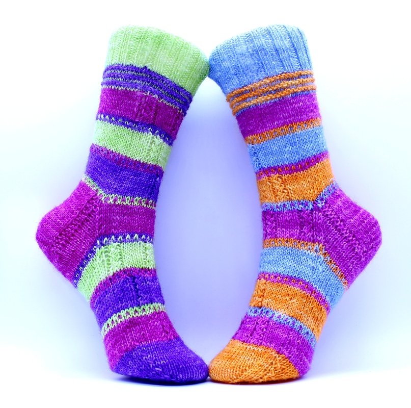 Zwei aufrecht stehende handgestrickte Socken mit bunten horizontalen Streifen auf hellem Hintergrund.
