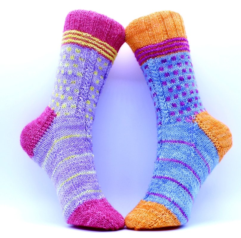 Zwei handgestrickte Socken in Lila, Pink, Blau und Orange mit Punkten, Streifen, Rippenbündchen und kontrastierenden Fersen