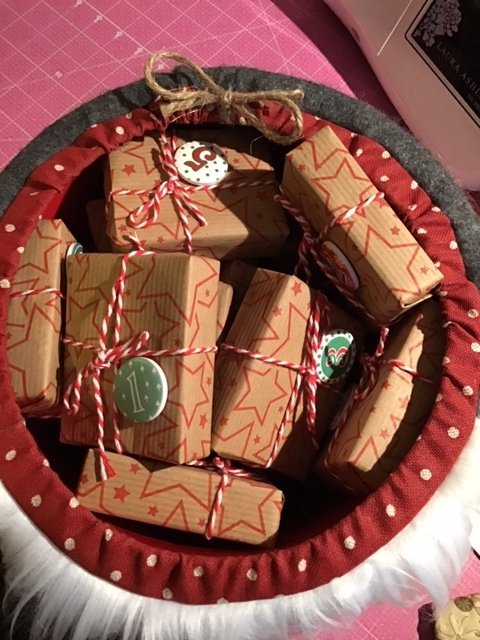 Rot gepunkteter Stoffkorb mit kleinen Stern-Kraftpapierpaketen, rot-weißem Garn und nummerierten Anhängern