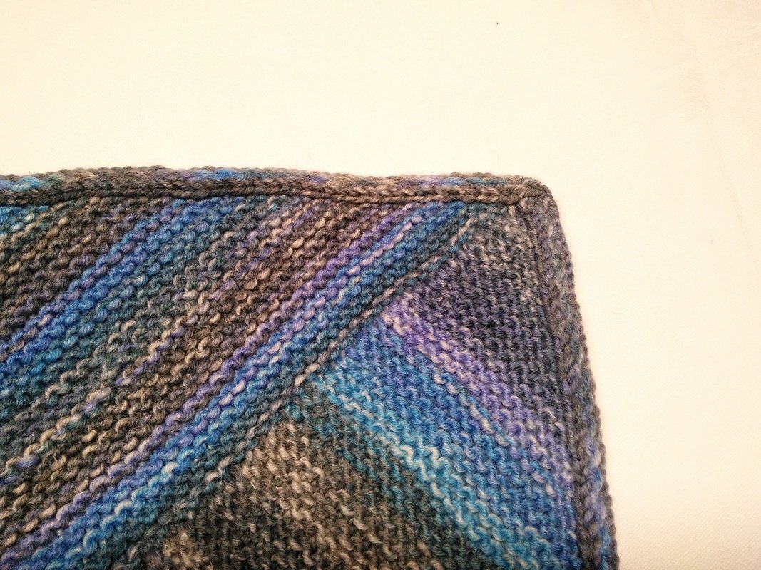 Eckdetail einer gestrickten Babydecke mit diagonalen kraus-rechts-Reihen in Blau, Grau und Violett