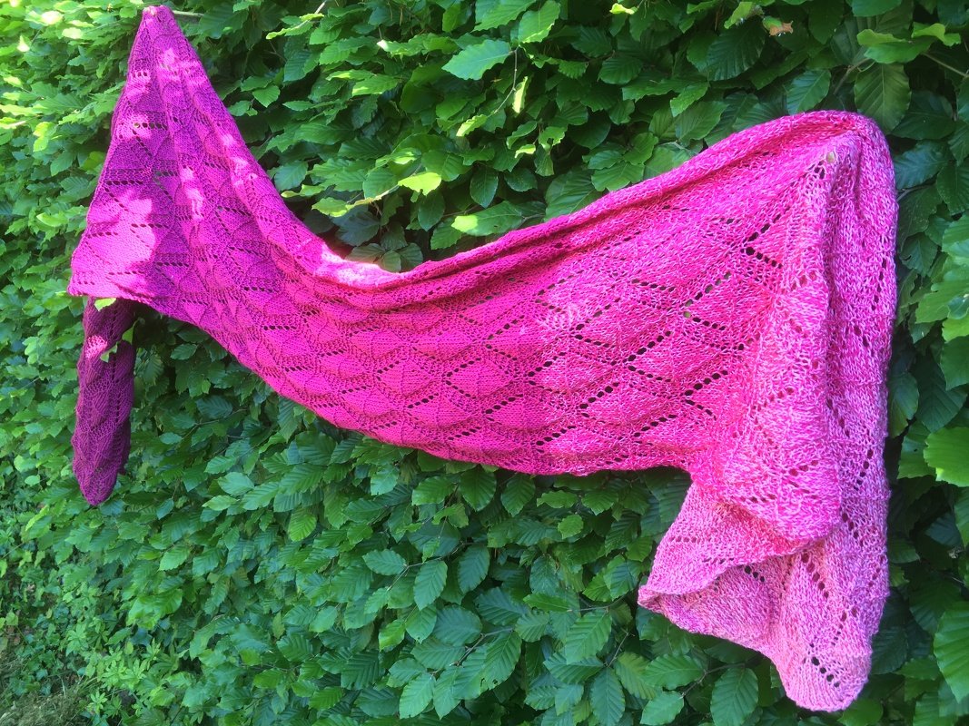 Asymmetrisches gestricktes Dreieckstuch in Pink mit Ajour-Blattmuster an grüner Hecke