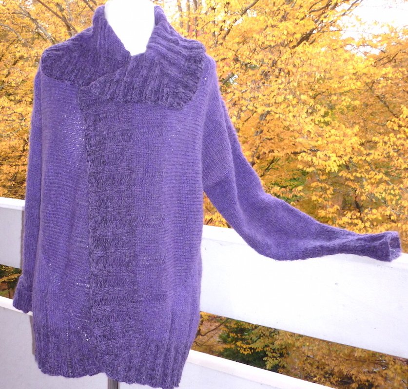 Lila gestrickte Damenjacke mit breitem geripptem Kragen auf Büste vor herbstlichem Laub