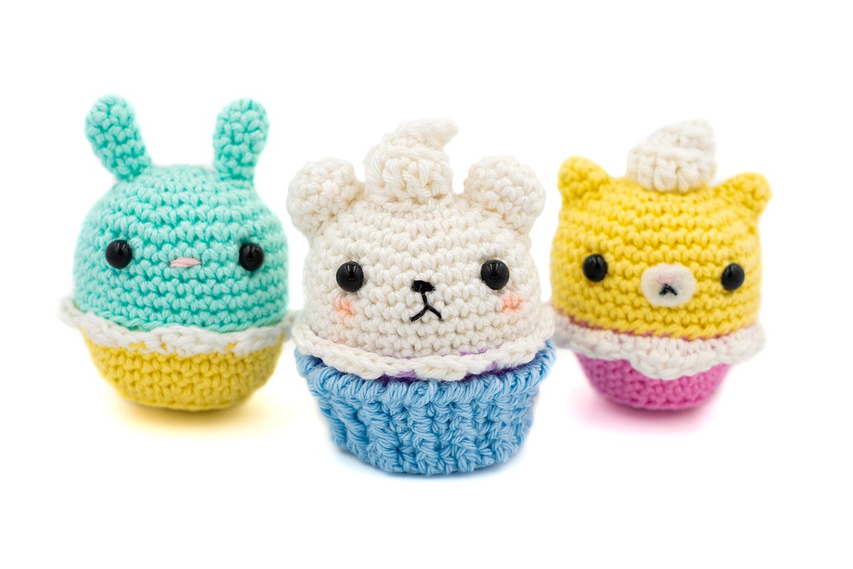 Drei gehäkelte Amigurumi‑Cupcakes in Mint, Creme und Gelb mit Hasen-, Bären- und Katzen‑Gesichtern