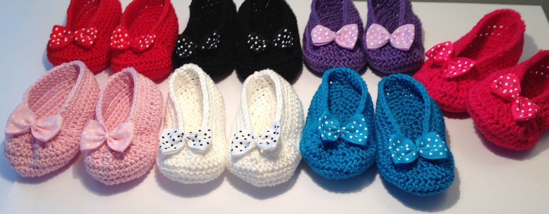 Aufgereihte gehäkelte Baby-Ballerinas in verschiedenen Farben mit Schleifenakzenten