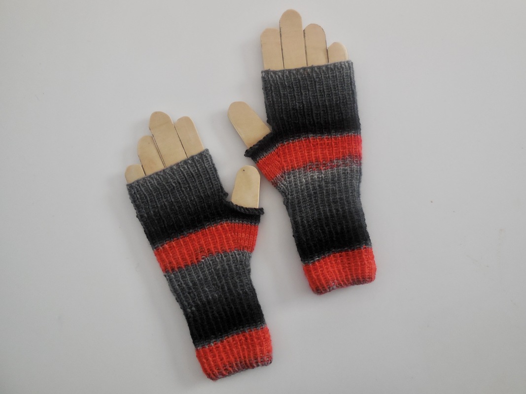 Gestrickte, fingerlose Handschuhe mit grauen, schwarzen und roten Streifen auf Holzhandformen.