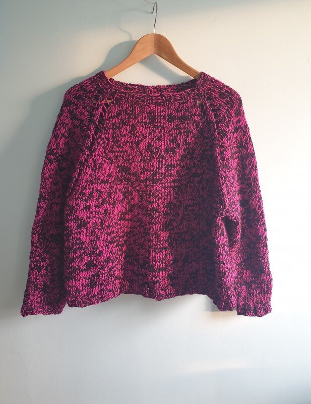 Magenta and black speckled knit sweater on a wooden hanger.