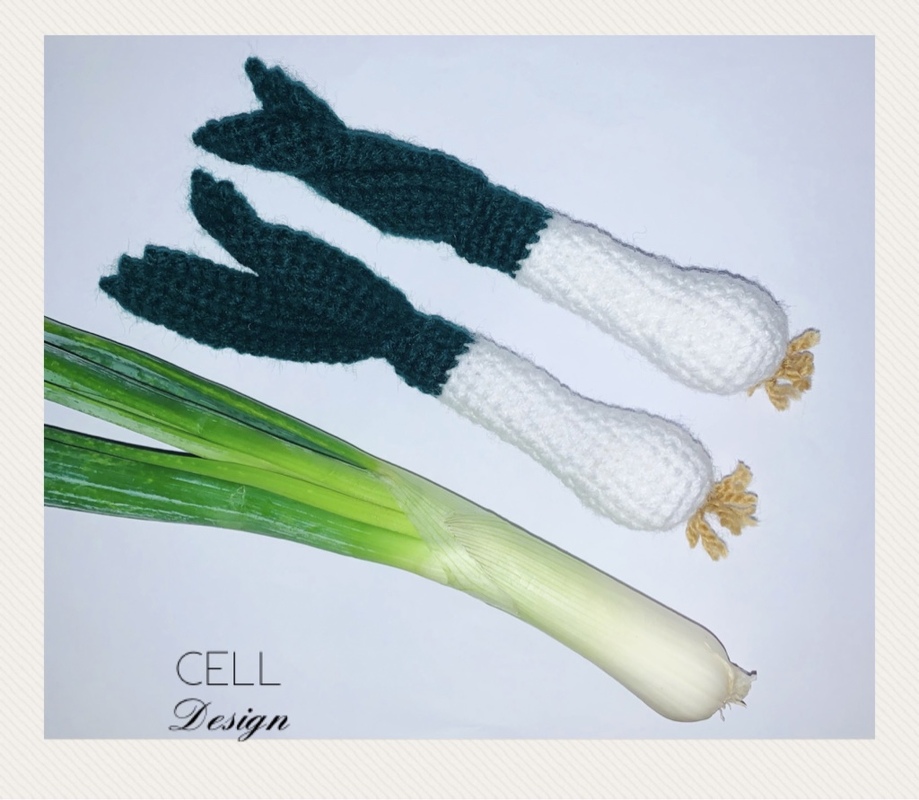 Zwei gehäkelte Frühlingszwiebeln in Weiß und Dunkelgrün, daneben eine echte Frühlingszwiebel zum Vergleich.