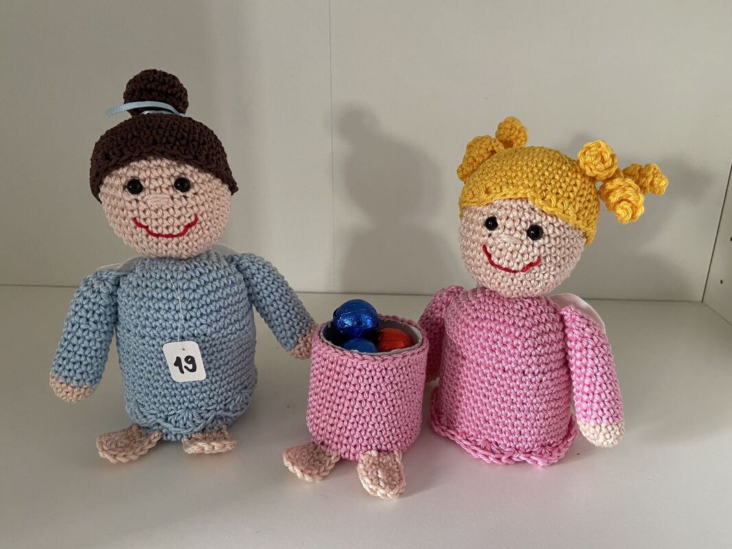 Zwei gehäkelte Puppen in Blau und Rosa mit kleinem rosa Körbchen und Kugeln, eine Figur mit Anhänger „19“