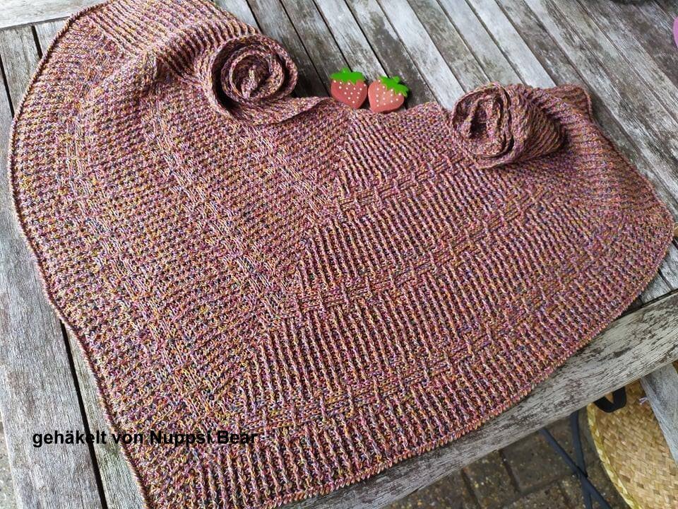 Nahaufnahme eines gehäkelten Dreieckstuchs mit Strukturmuster in melierten Rosa- und Brauntönen auf Holzuntergrund