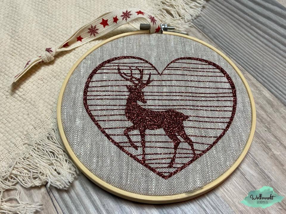 Stickrahmen mit glitzerndem Hirsch im herzförmigen Rahmen auf hellem Stoff