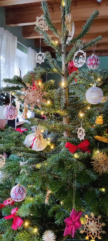 Tannenbaum mit gehäkelten Spitzenkugeln, Strohsternen, roten Schleifen und Lichterkette