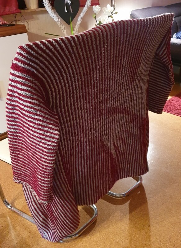 Gestreifter Strickpullover in Rot und Grau über Stuhllehne gelegt