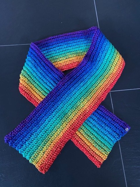 Gehäkelter Regenbogenschal mit Rippstruktur, überkreuzt auf dunklem Boden