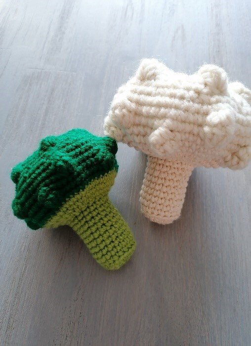 Gehäkelter grüner Brokkoli und weißer Blumenkohl auf hellem Holz