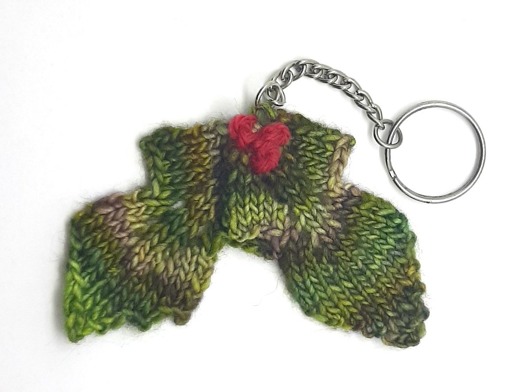 Gestrickter Stechpalmen-Schlüsselanhänger mit roten Beeren an Metallring auf weißem Hintergrund.