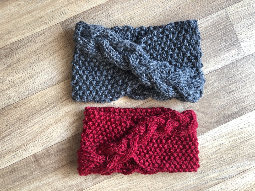Zwei gestrickte Stirnbänder in Grau und Rot mit Zopfmuster auf Holzboden