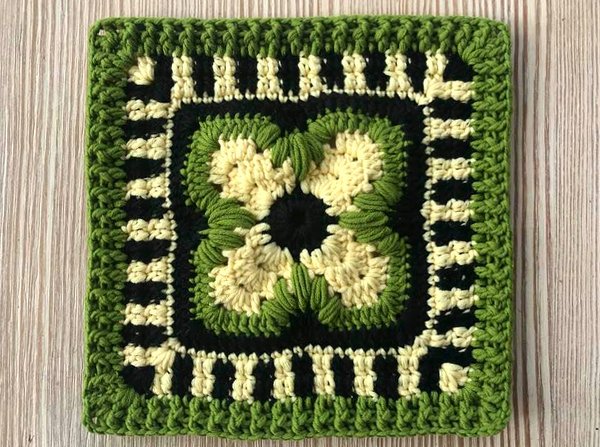 Quadratisches Häkelquadrat in Grün, Schwarz und Beige mit floralem Zentrum und gestreiftem Rand.