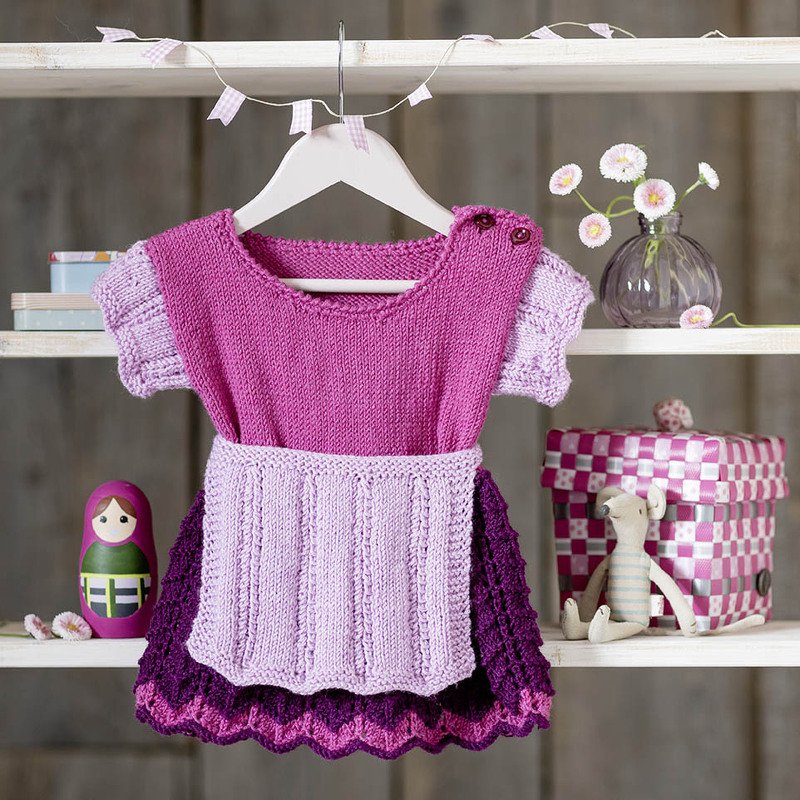 Gestricktes Babykleid in Rosa und Lila mit Schürze an einem Kleiderbügel