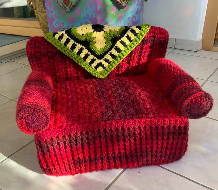 Rotes gehäkeltes Katzensofa mit gerollten Armlehnen und grün-schwarzem Granny-Deckchen