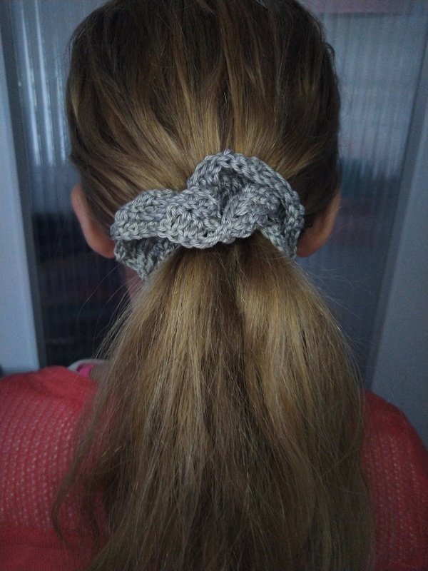 Rückansicht einer Person mit blondem Pferdeschwanz, gehalten von einem grauen gehäkelten Scrunchie.