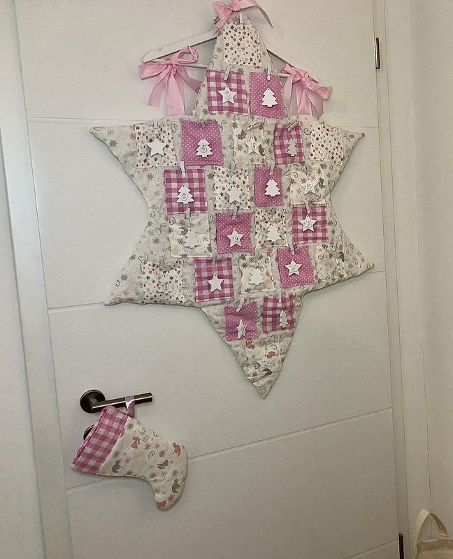 Gepatchter sternförmiger Adventskalender-Wandbehang in Rosa und Beige mit nummerierten Täschchen, weißen Holzanhängern und Stoffstiefel am Türgriff