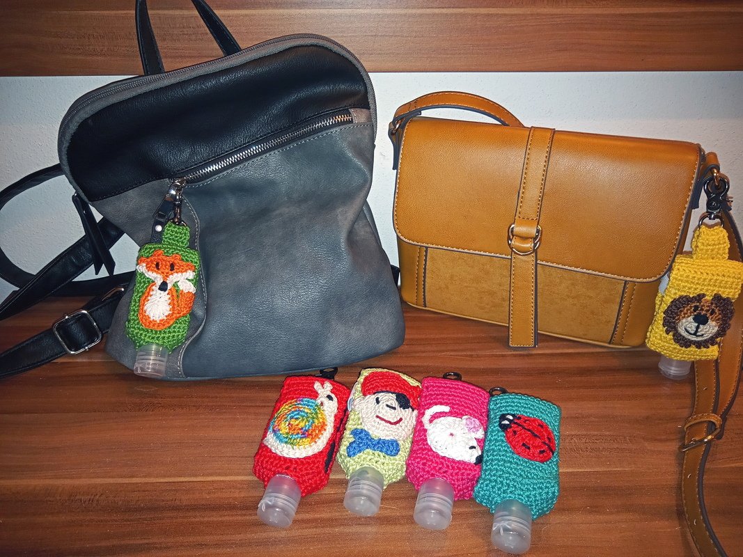 Mehrere bunte, gehäkelte Flaschenhüllen als Taschenanhänger; zwei Hüllen sind an Lederhandtaschen befestigt