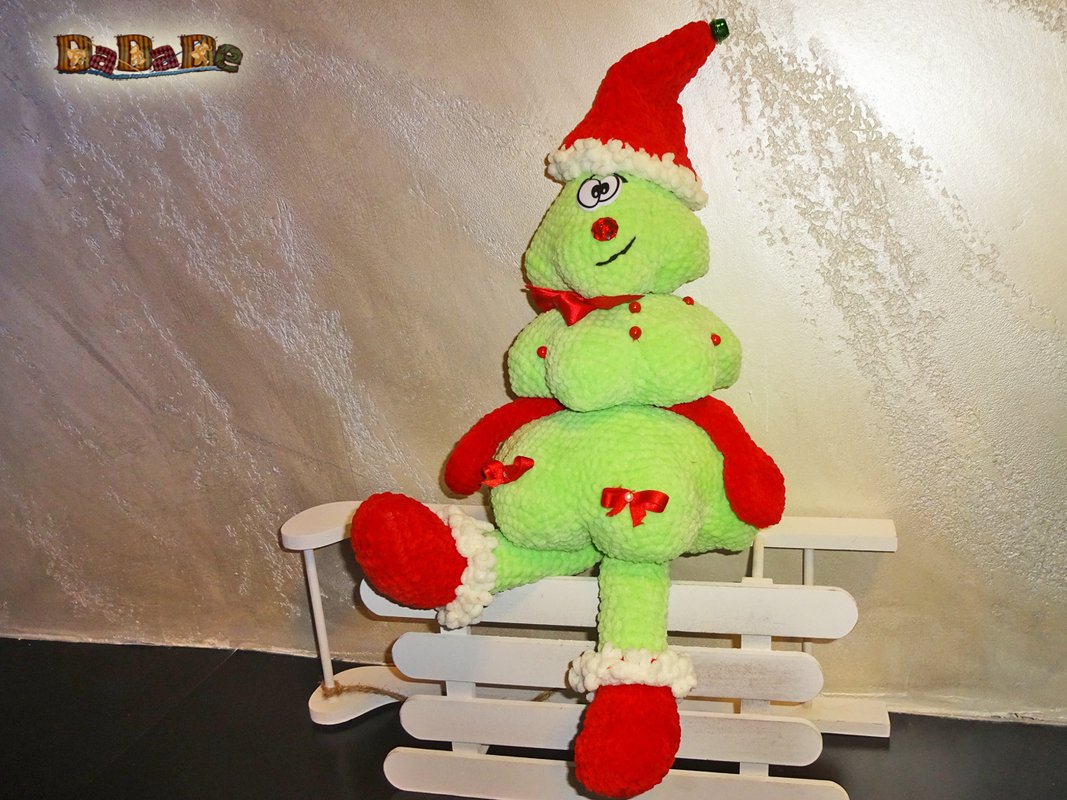 Grünes gehäkeltes Amigurumi mit roter Weihnachtsmütze auf weißem Schlitten