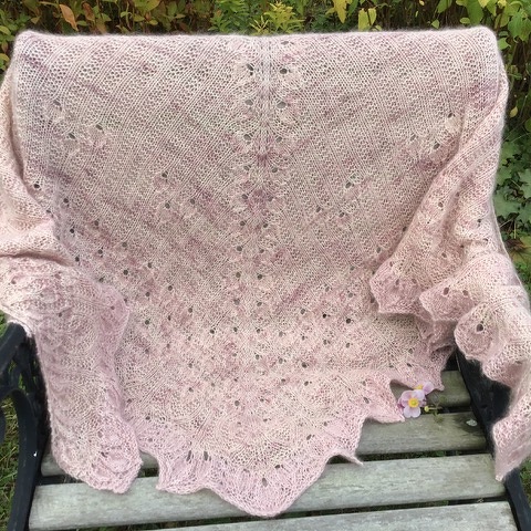 Gestricktes rosafarbenes Dreieckstuch mit Spitzen- und Lochmuster auf einer Holzbank