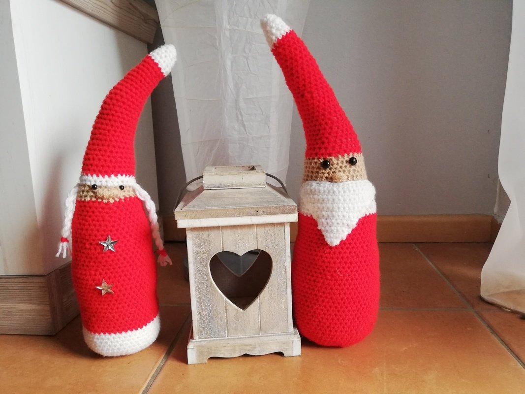 Zwei gehäkelte Weihnachtswichtel in Rot und Weiß neben einer Holzlaterne