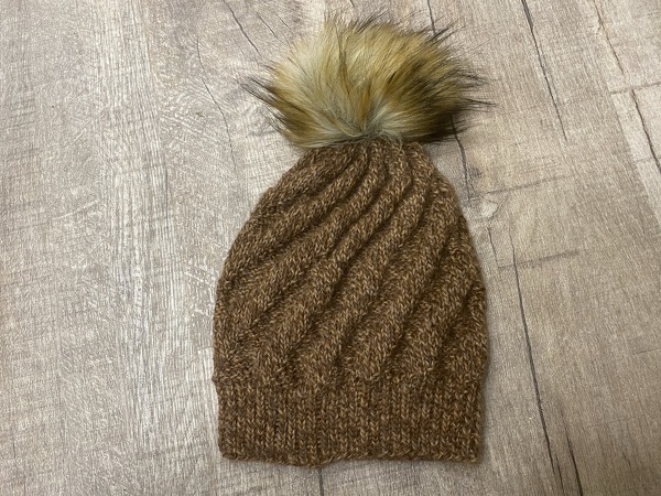 braune gestrickte Beanie mit großem Bommel auf Holzfußboden