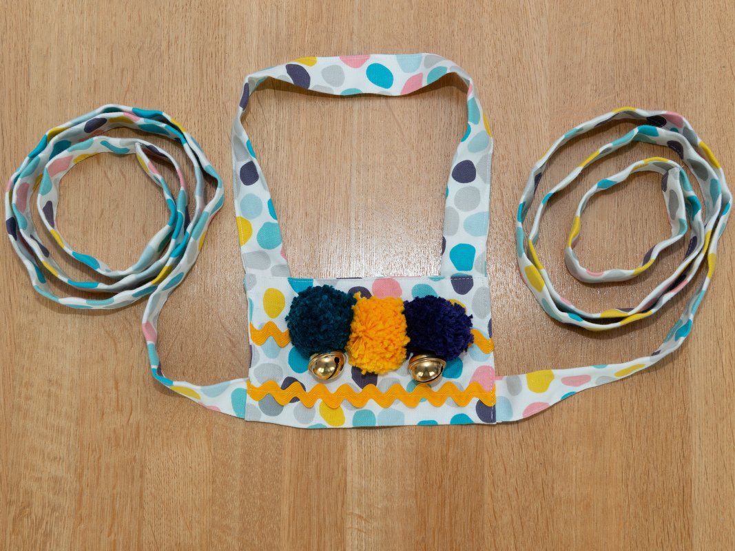 Bunter Musikgürtel mit drei Pompons, zwei Glöckchen und Zackenborte auf Holzboden