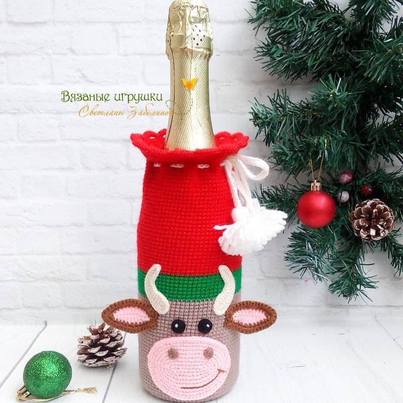 Gehäkelte Flaschenhülle in Rot, Grün und Beige mit Kuhgesicht vor weihnachtlicher Dekoration