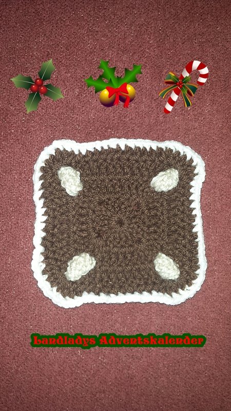 Braunes gehäkeltes Quadrat mit weißem Zierrand und vier hellen Eckapplikationen, auf einem rötlich-texturierten Hintergrund, dekoriert mit weihnachtlichen Stickern oben.