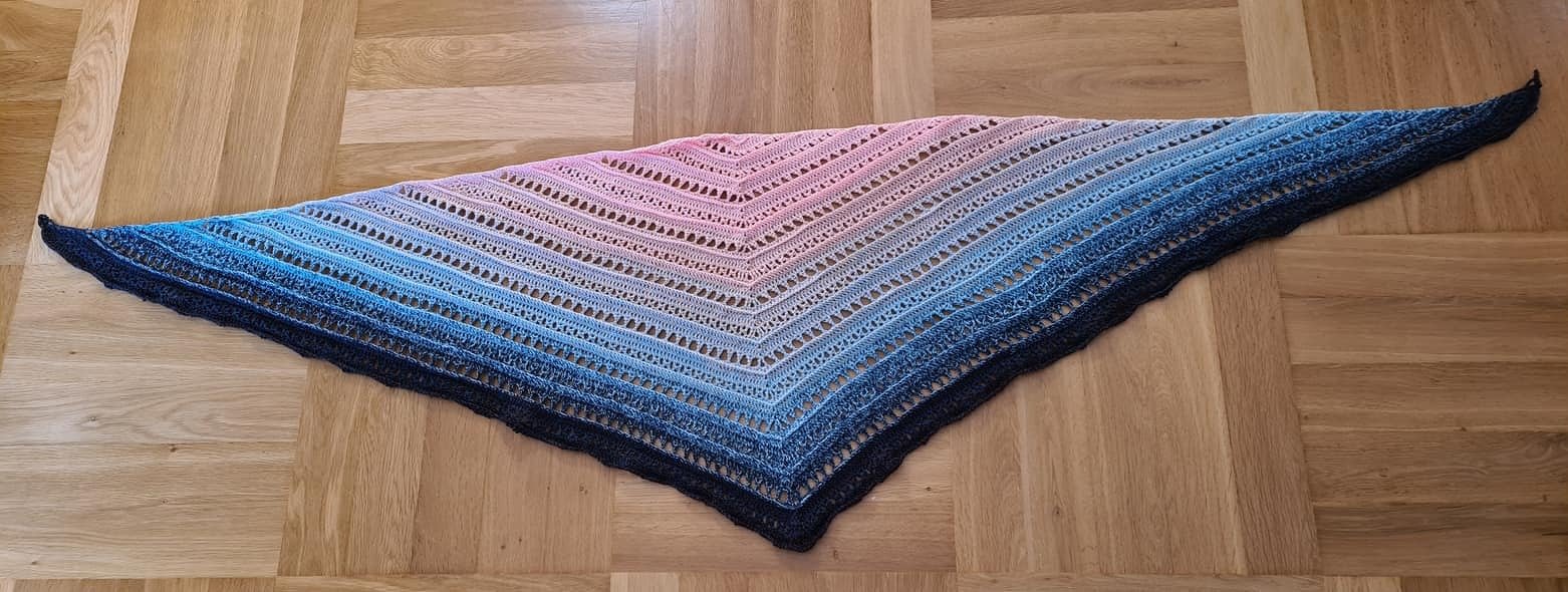 Gehäkeltes Dreieckstuch mit rosa‑blauem Farbverlauf auf Parkettboden