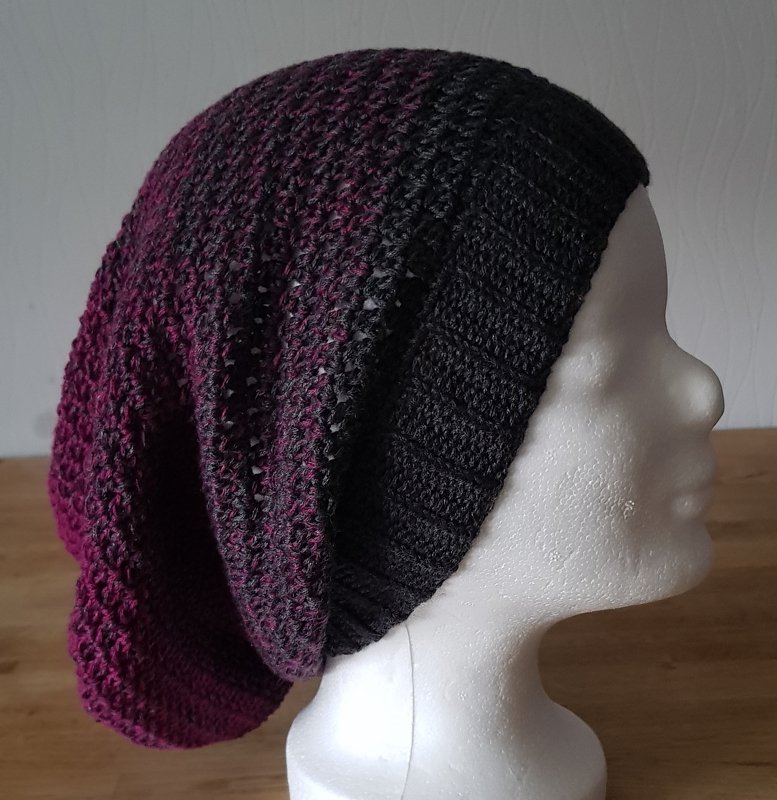 Gehäkelte Longbeanie mit Farbverlauf von Schwarz zu Magenta auf einem weißen Schaufensterpuppenkopf.
