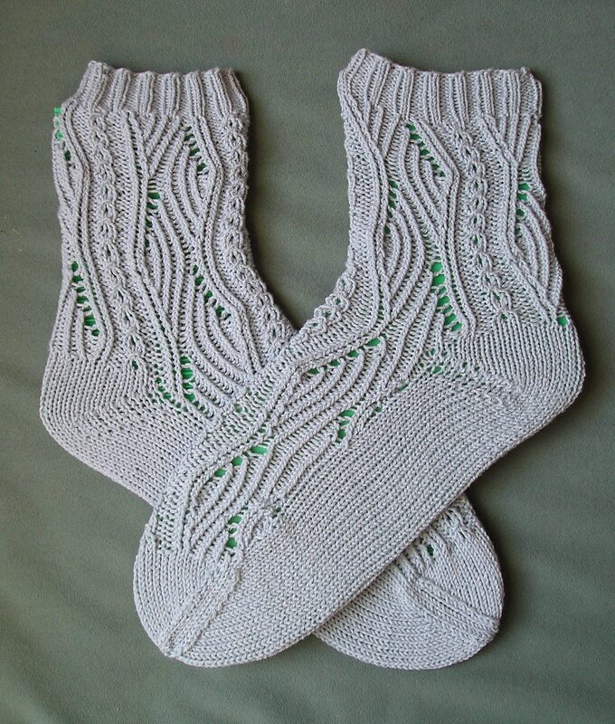 Gekreuztes Paar hellgrauer gestrickter Damensocken mit Ajour- und Zopfmuster auf grünem Untergrund