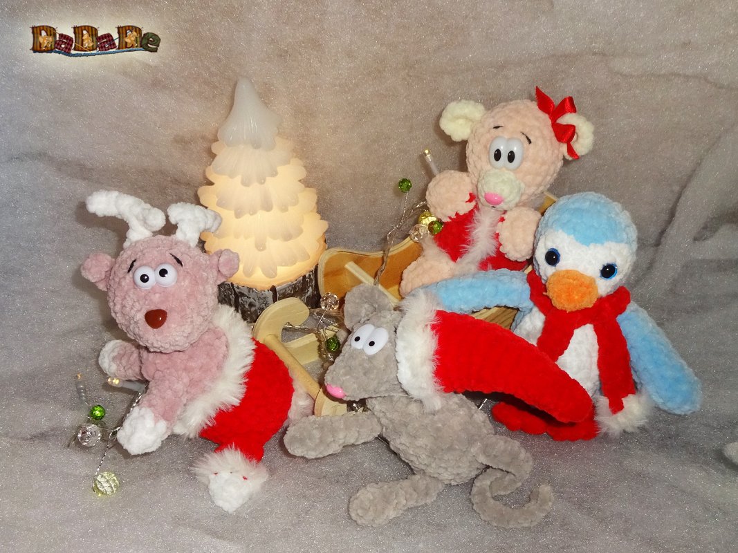 Vier gehäkelte Weihnachts-Kuscheltiere mit roten Schals, Holzschlitten und beleuchtetem Baum