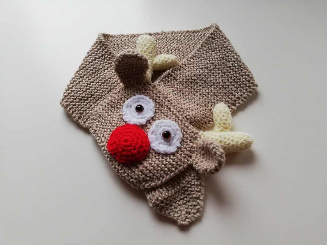 Beigefarbener gestrickter Babyschal im Rentier-Design mit roter Pompon-Nase und applizierten Augen.