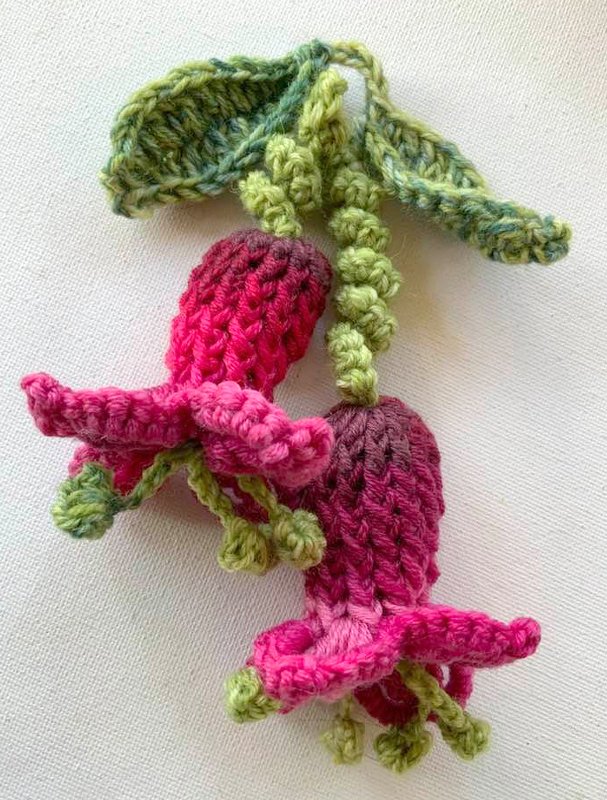 Zwei gehäkelte Fuchsienblüten in Pink-Violett mit grünen Blättern
