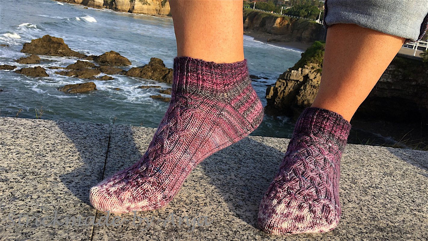 Nahaufnahme knöchelhoher gestrickter Socken in lila Melange mit Zopfmuster