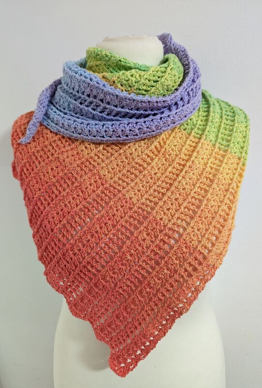 Triangle crochet shawl in coral, orange, yellow, green and lavender gradient draped on a mannequin