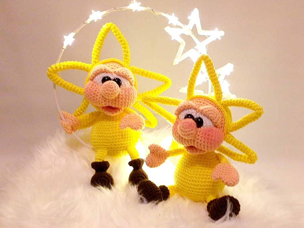 Two yellow crochet star amigurumi dolls with pink faces and brown boots on white fur beside star-shaped string lights