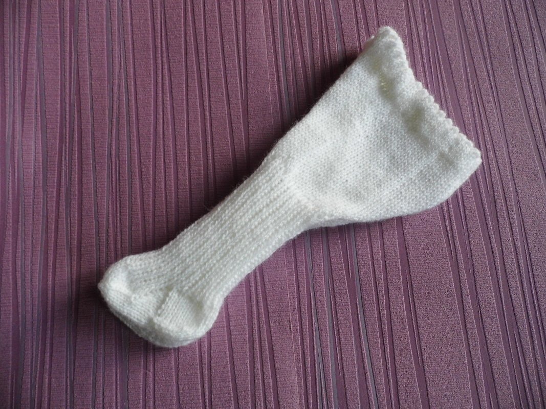 Handgestrickte weiße Babysocke auf violettem, geriffeltem Stoff