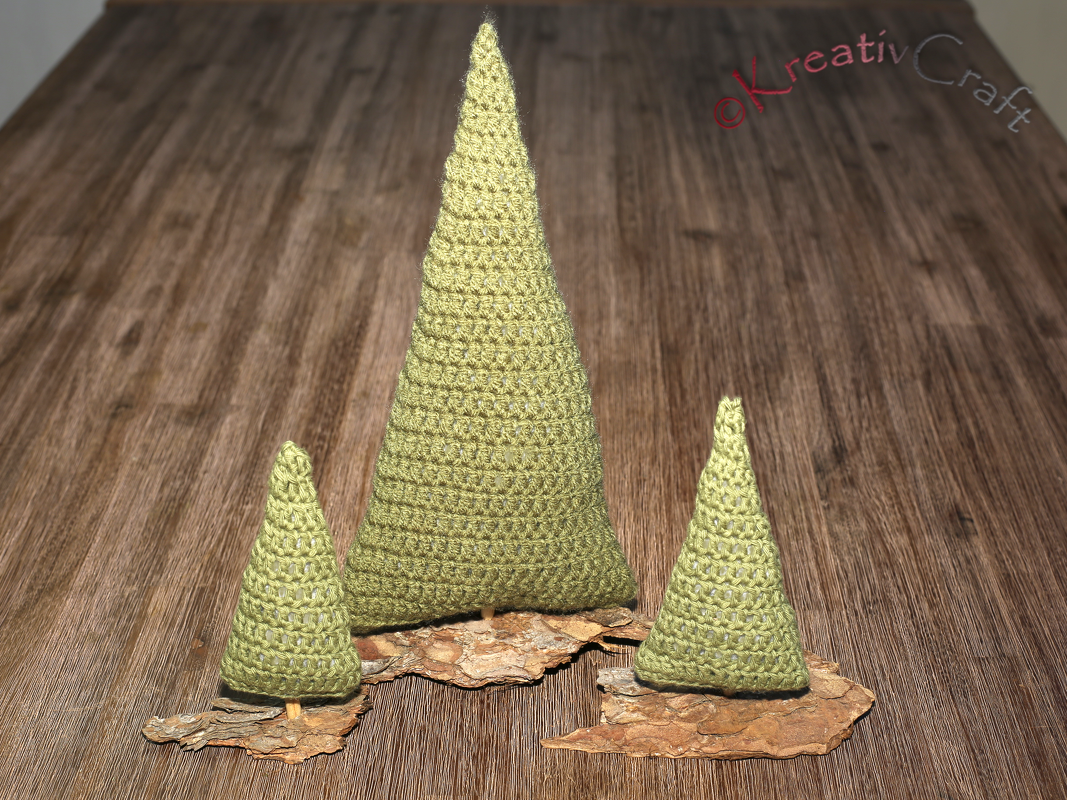 Three green crocheted cone Christmas trees on bark on a wooden table