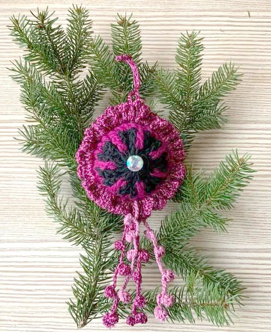 Gehäkeltes Ornament in Lila und Schwarz mit Perle an einem Tannenzweig
