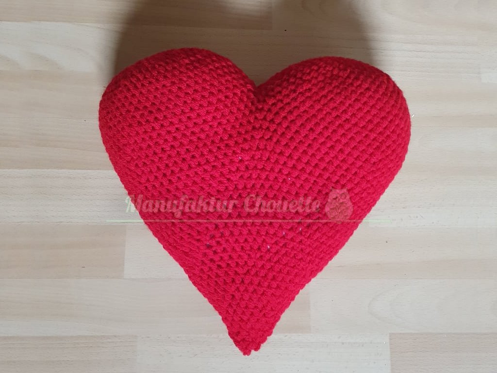 Kräftig rotes herzförmiges Häkelkissen auf Holzfläche