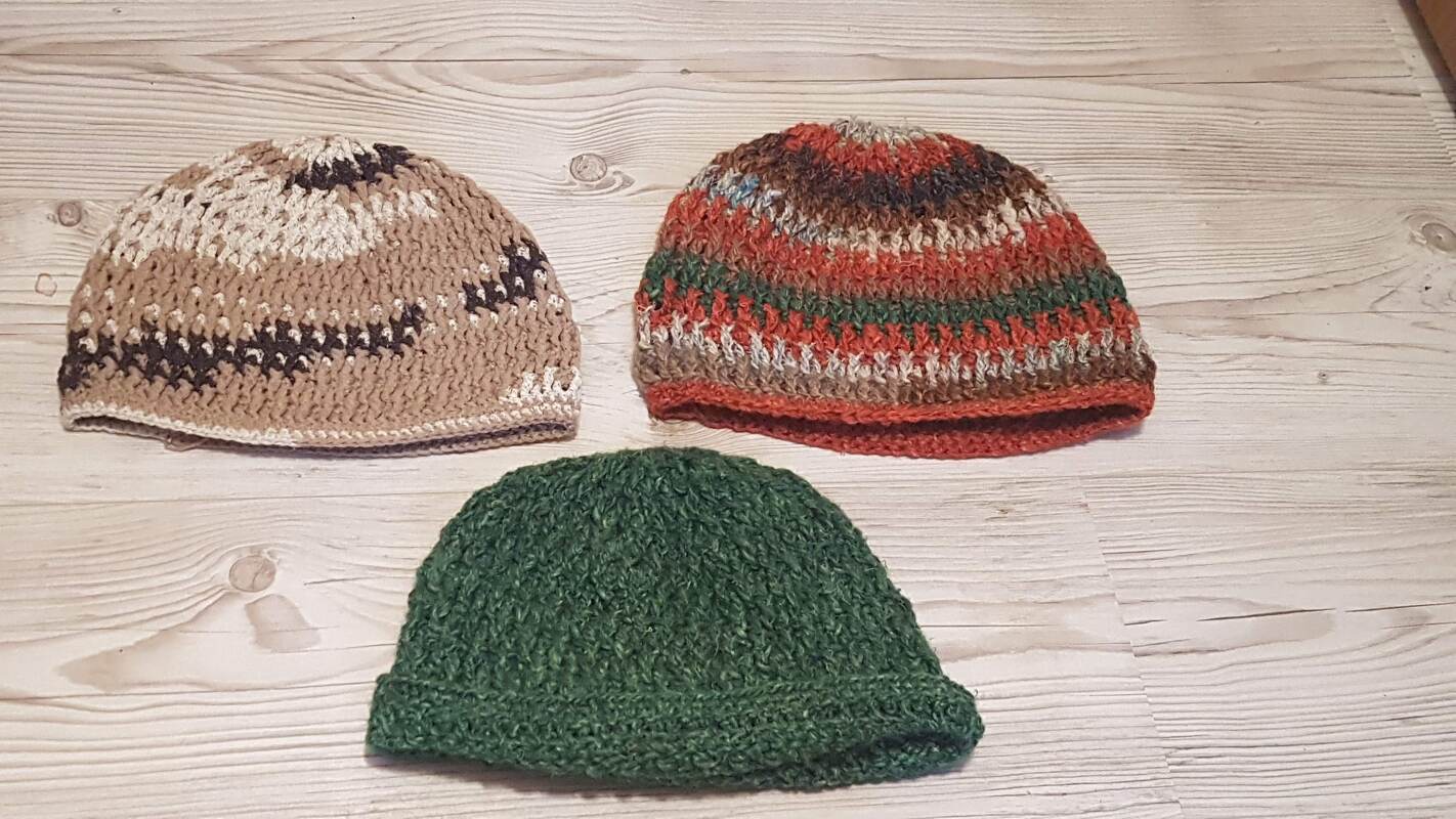 Drei gehäkelte Mützen in Beige, gestreift und Grün auf hellem Holz