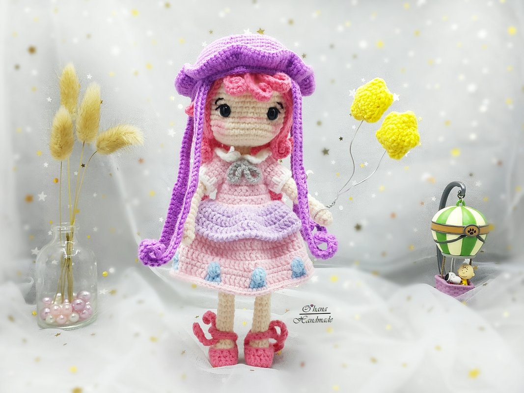 Amigurumi crochet doll with pink curls, pastel pink dress, purple hat, holding yellow star balloons